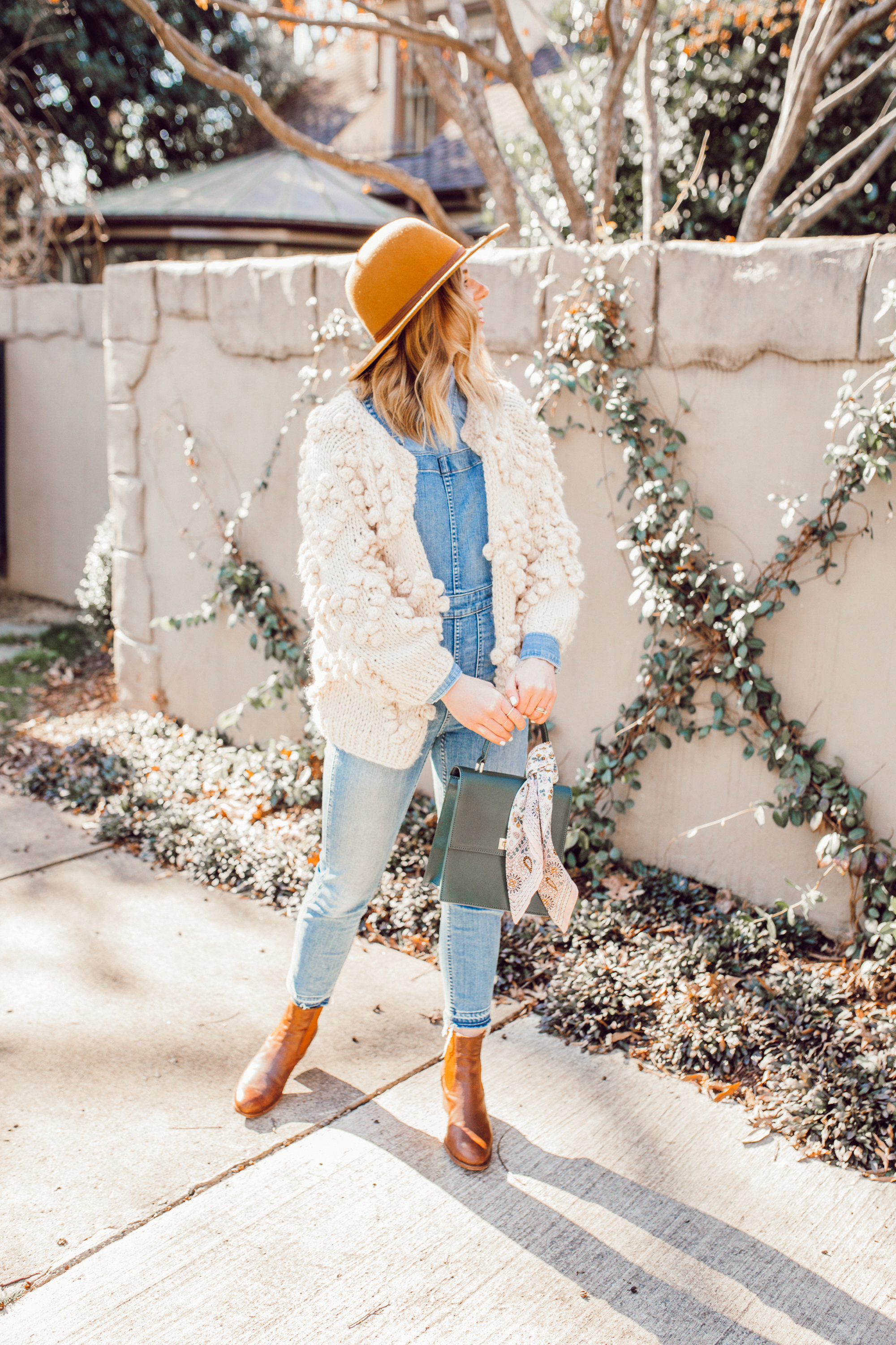 The Importance of Buying Pieces You LOVE - Even If Trendy featured on top US life and style blog Louella Reese| Image of a woman wearing Chicwish Knit Your Love Cardigan, Madewell Overalls, Yellow Wool Hat, Ariat Two24 Wilder Boots, and Neely & Chloe Ladylike Handbag.