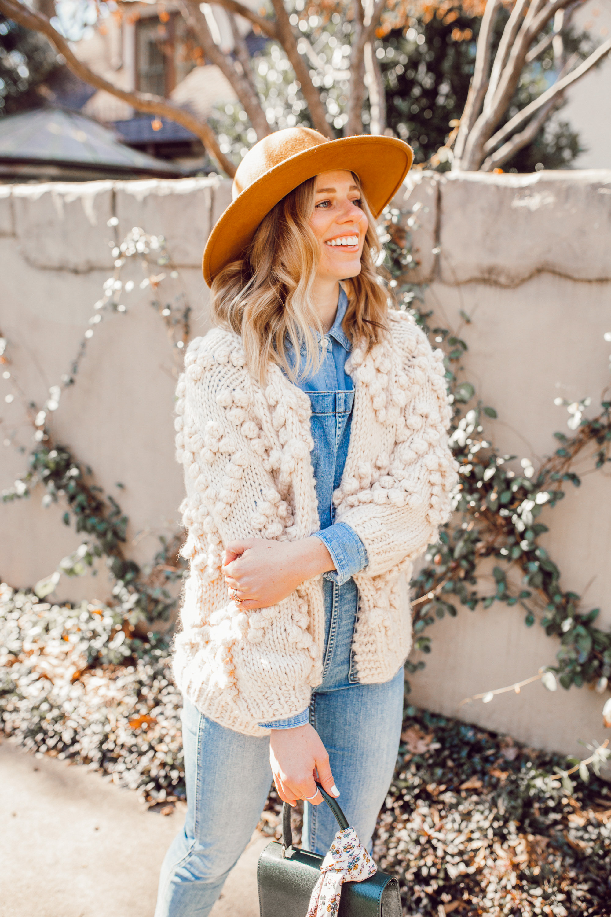 The Importance of Buying Pieces You LOVE - Even If Trendy featured on top US life and style blog Louella Reese| Image of a woman wearing Chicwish Knit Your Love Cardigan, Madewell Overalls, Yellow Wool Hat, Ariat Two24 Wilder Boots, and Neely & Chloe Ladylike Handbag.